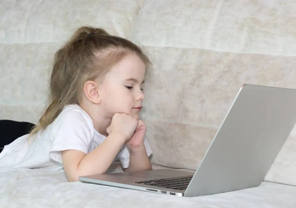 A little girl laying on the bed looking at her laptop