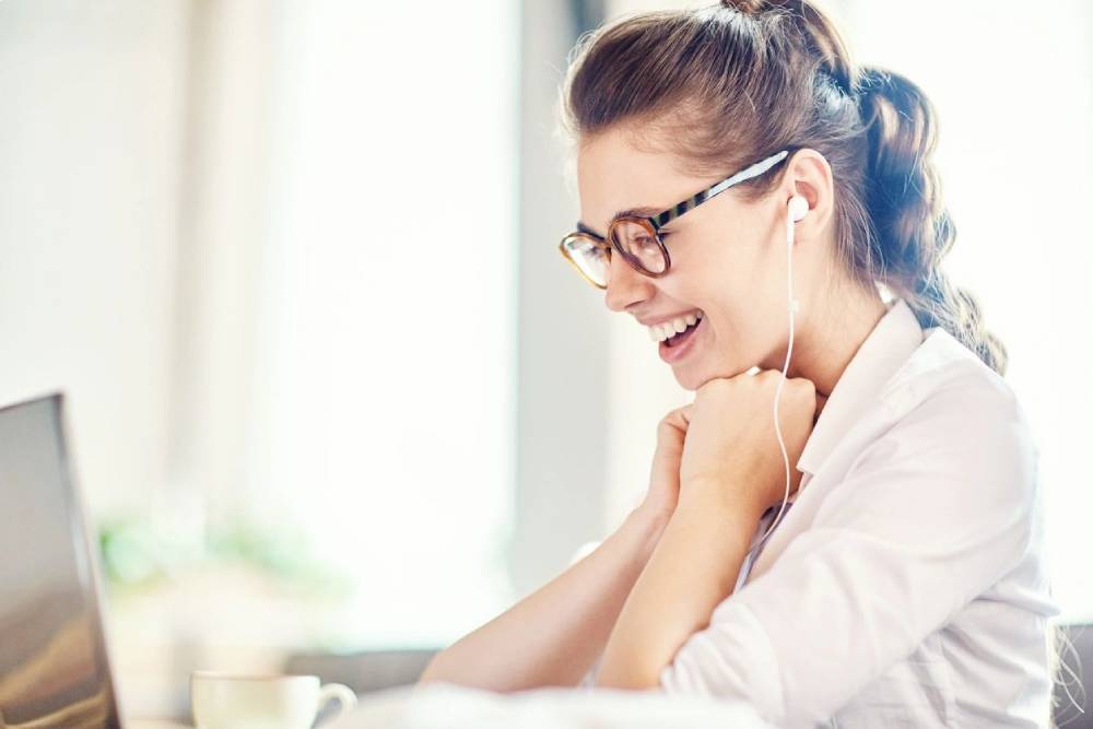 A woman with glasses is smiling and listening to music.