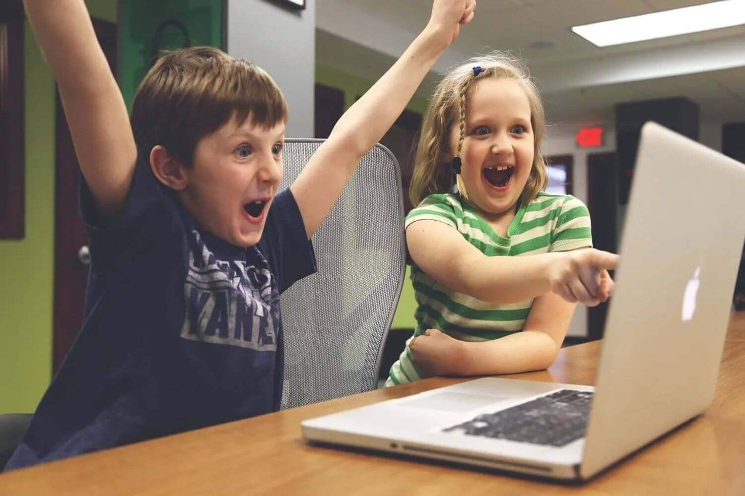 Two children sitting at a table with a laptop